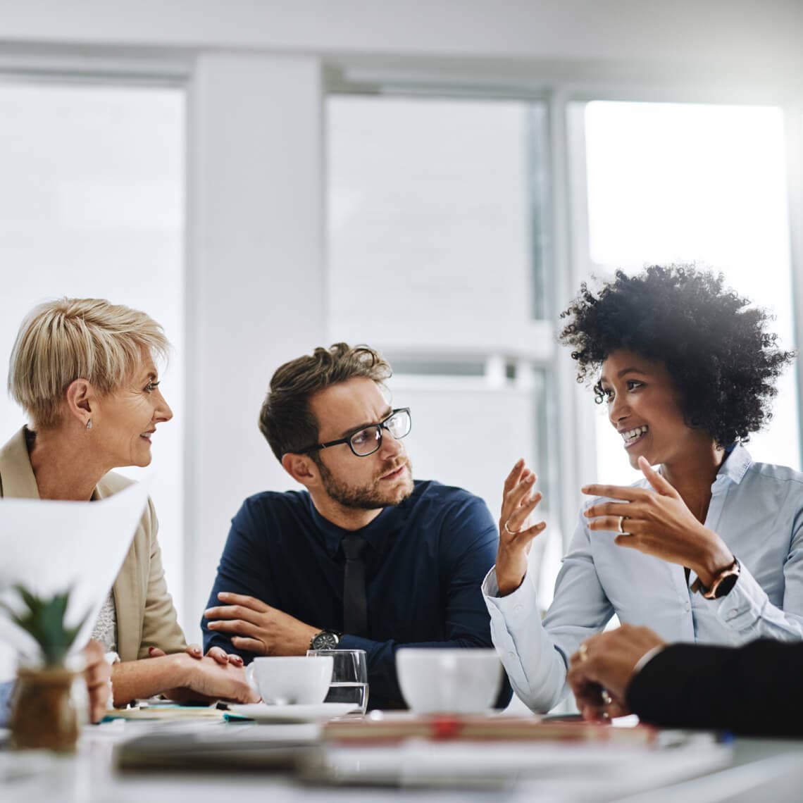 three coworkers talking in well lit office, sitting at at table