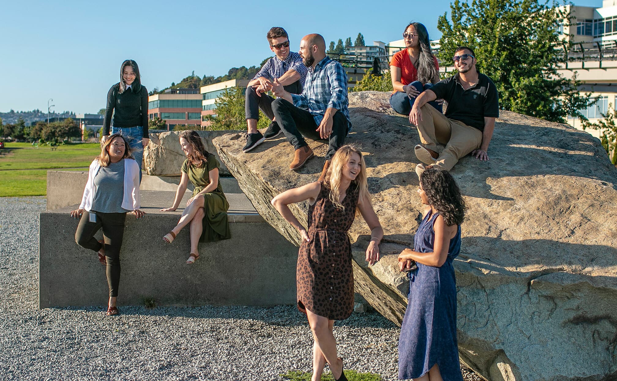 group of employees sitting outside talking on a rock