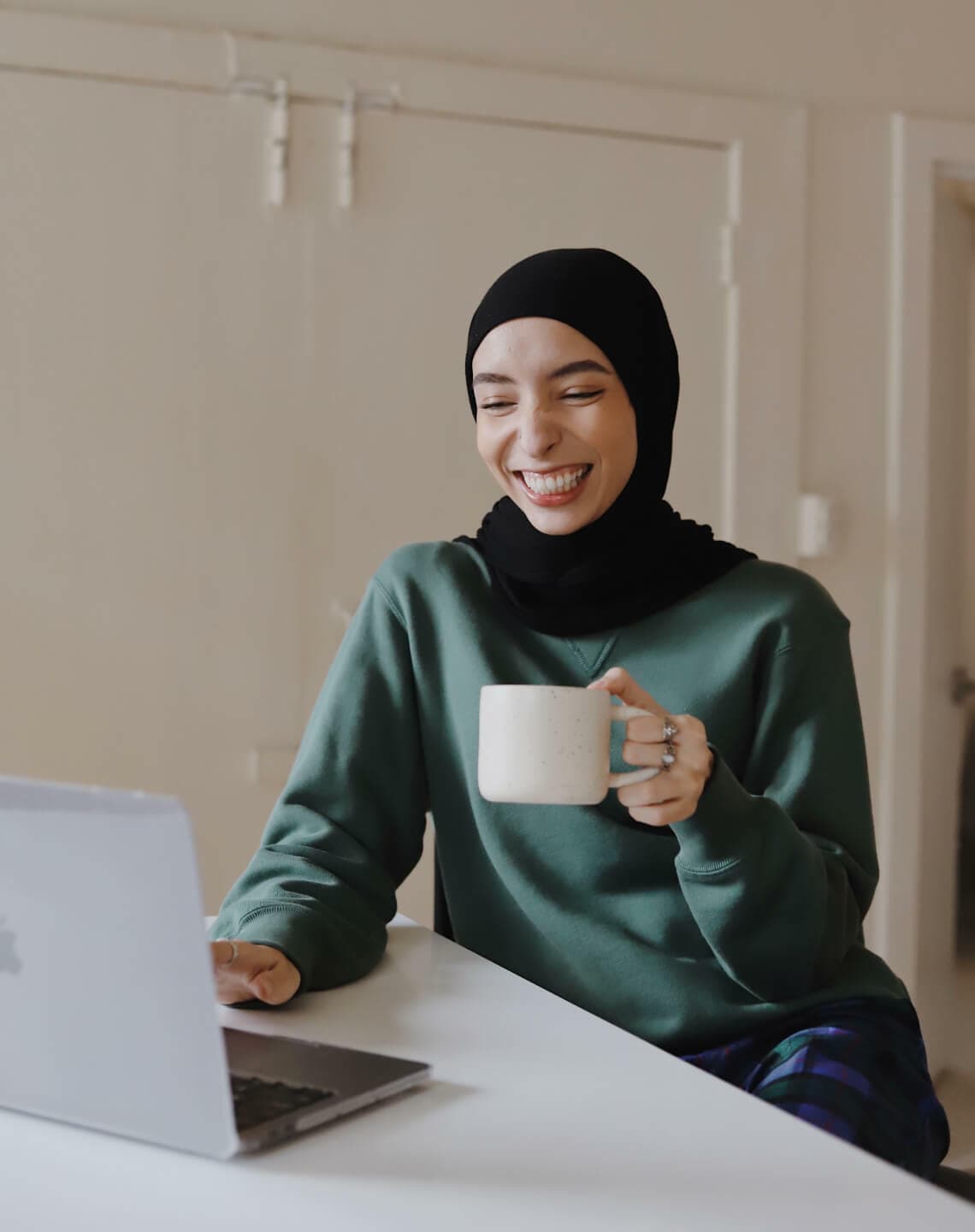 Woman working on laptop smiling and holding up of coffee