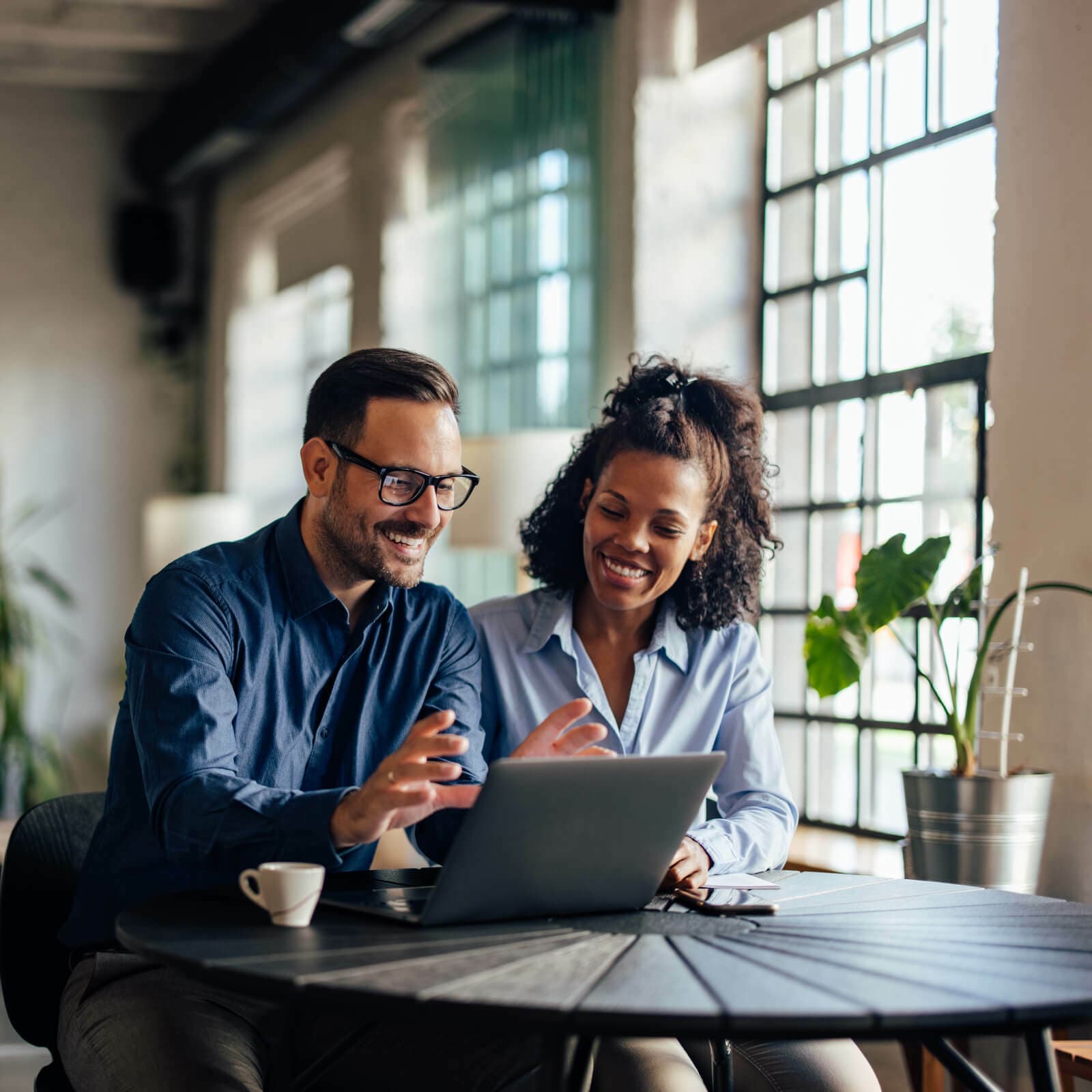 two sales leaders in an office, talking and working on a laptop